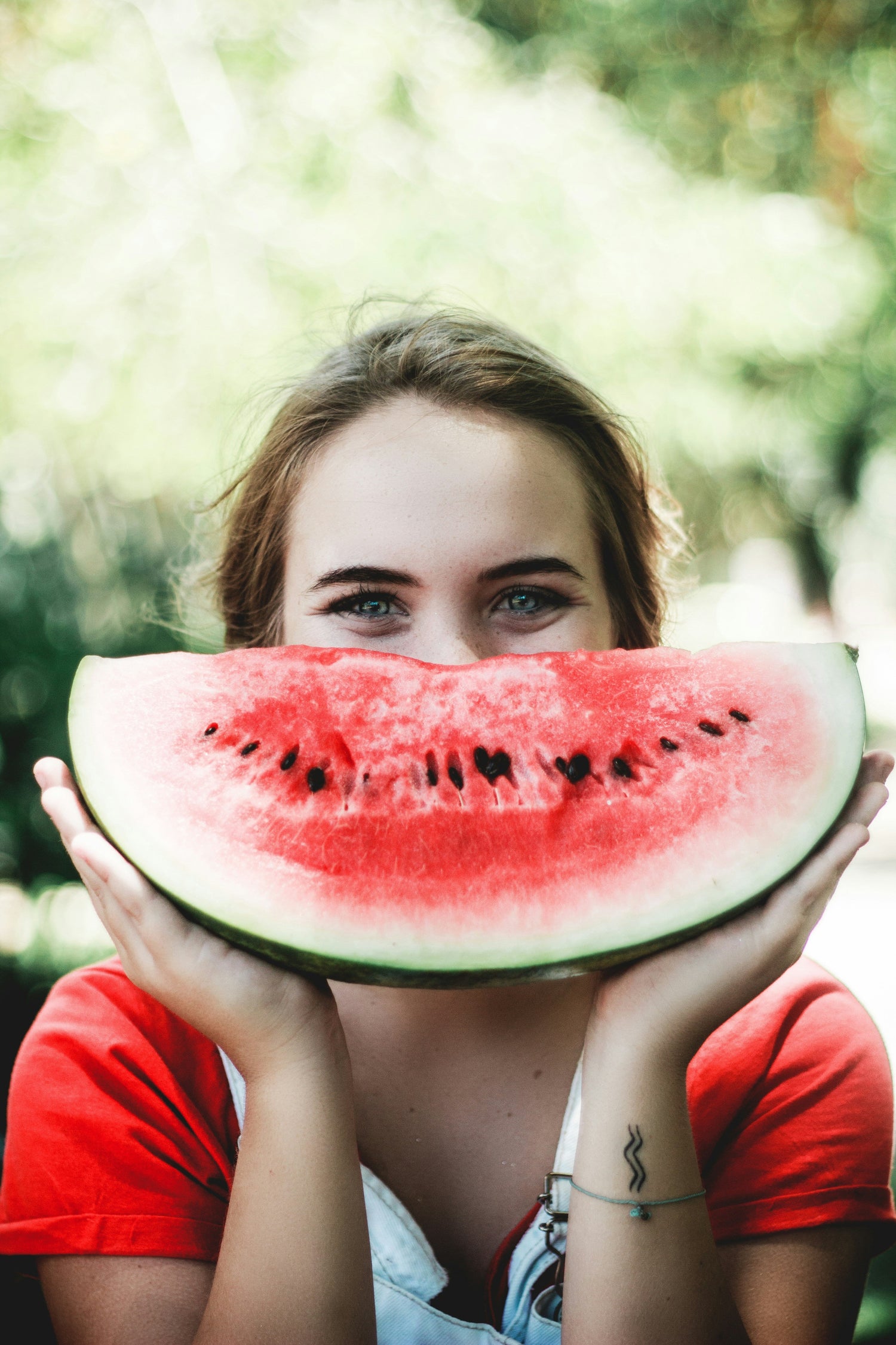 Mujer de ojos azules sosteniendo una sandía en frente de su rostro como si la sandía fuera su sonrisa | ProteinasMedellin.com